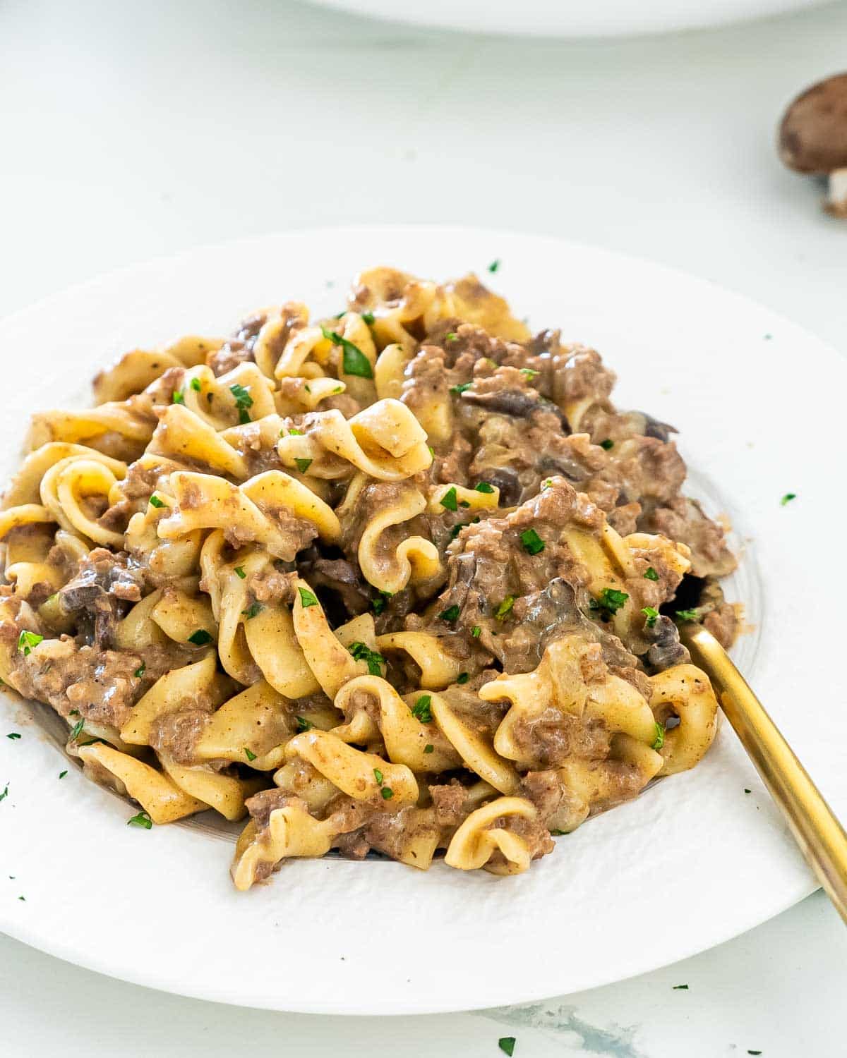 beef stroganoff on a white plate with a golden fork.