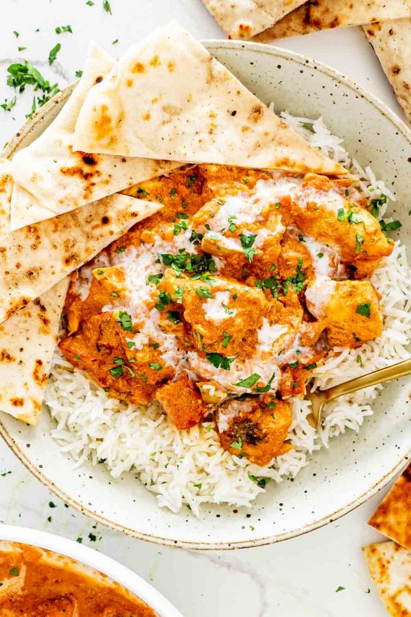 chicken tikka masala in a plate with rice and garnished with cilantro.
