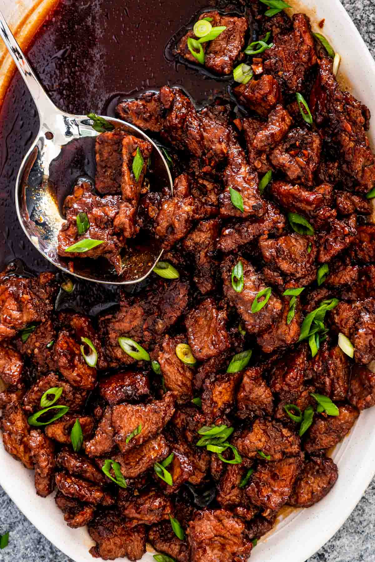 mongolian beef on a white serving platter with a serving spoon inside.