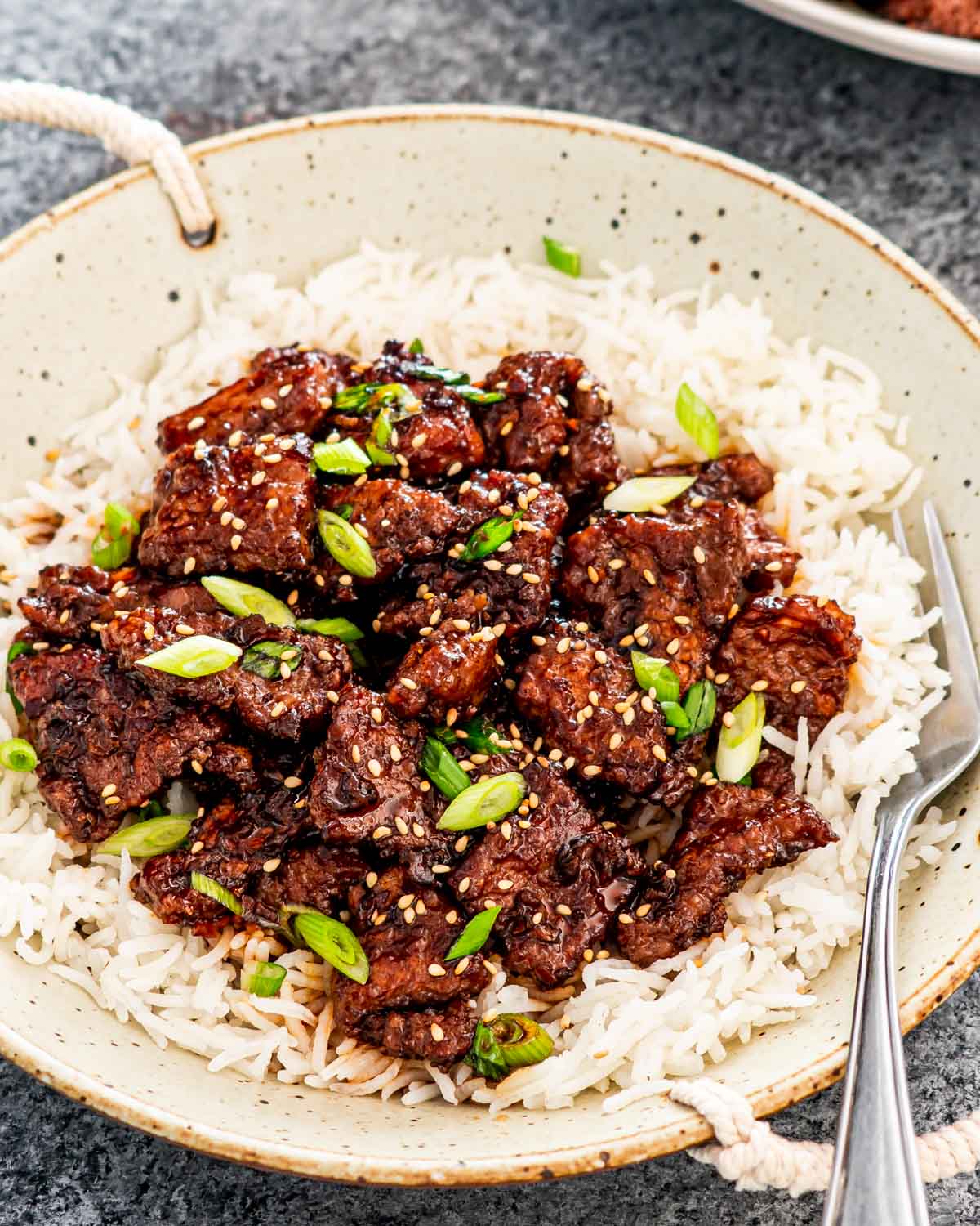 mongolian beef over a bed of rice garnished with green onions and sesame seeds.