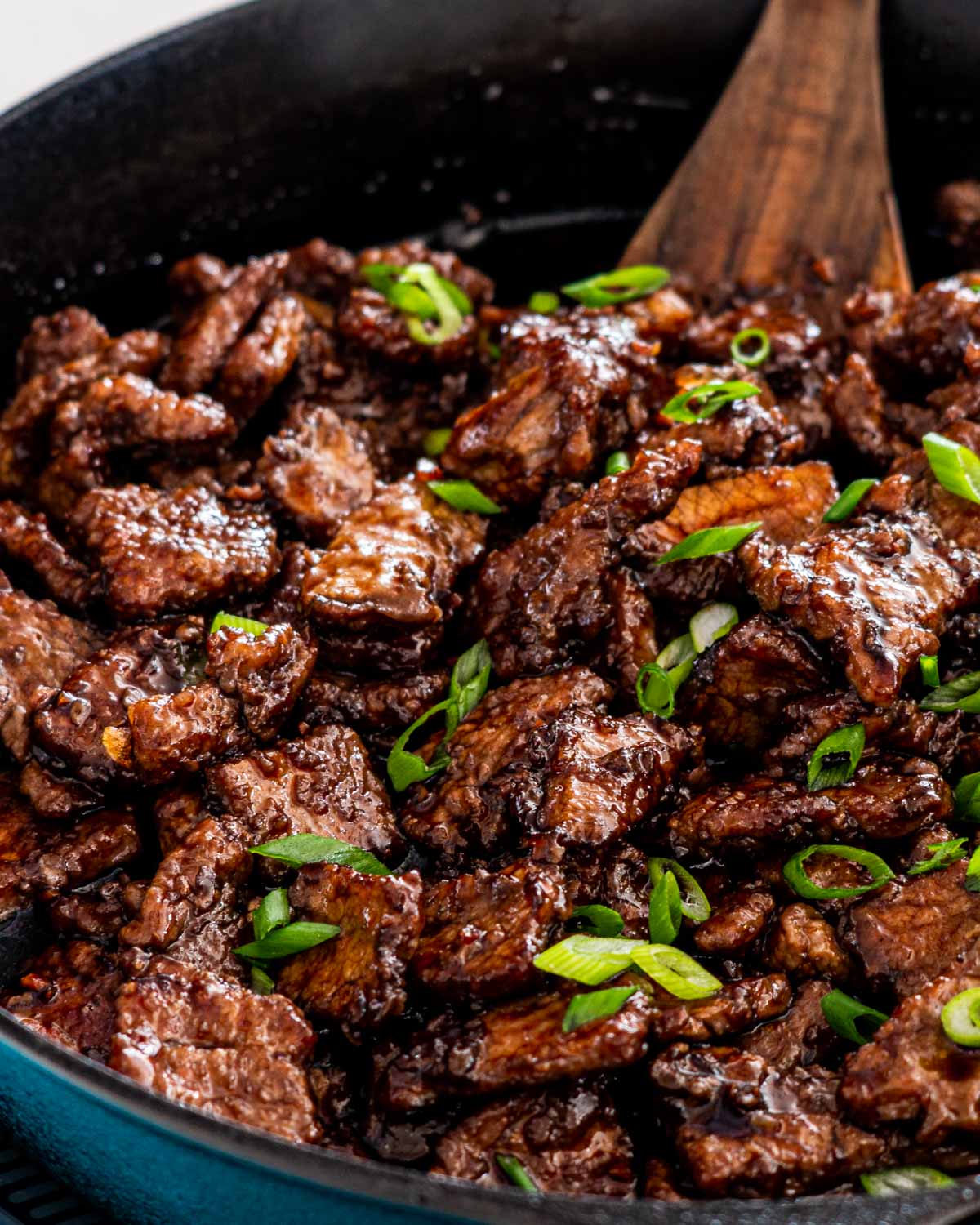 mongolian beef in a black skillet with a wooden spatula inside.