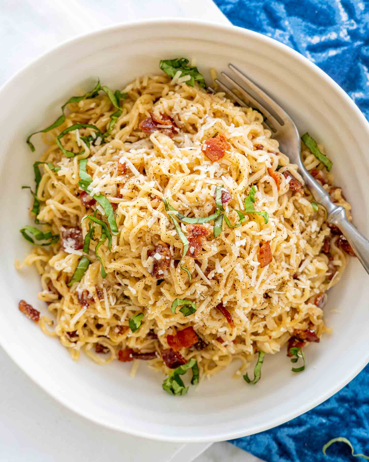 a bowl full of ramen carbonara garnished with basil.