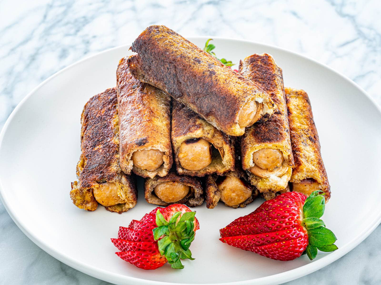 Sausage French Toast Roll Ups on a white plate garnished with strawberries