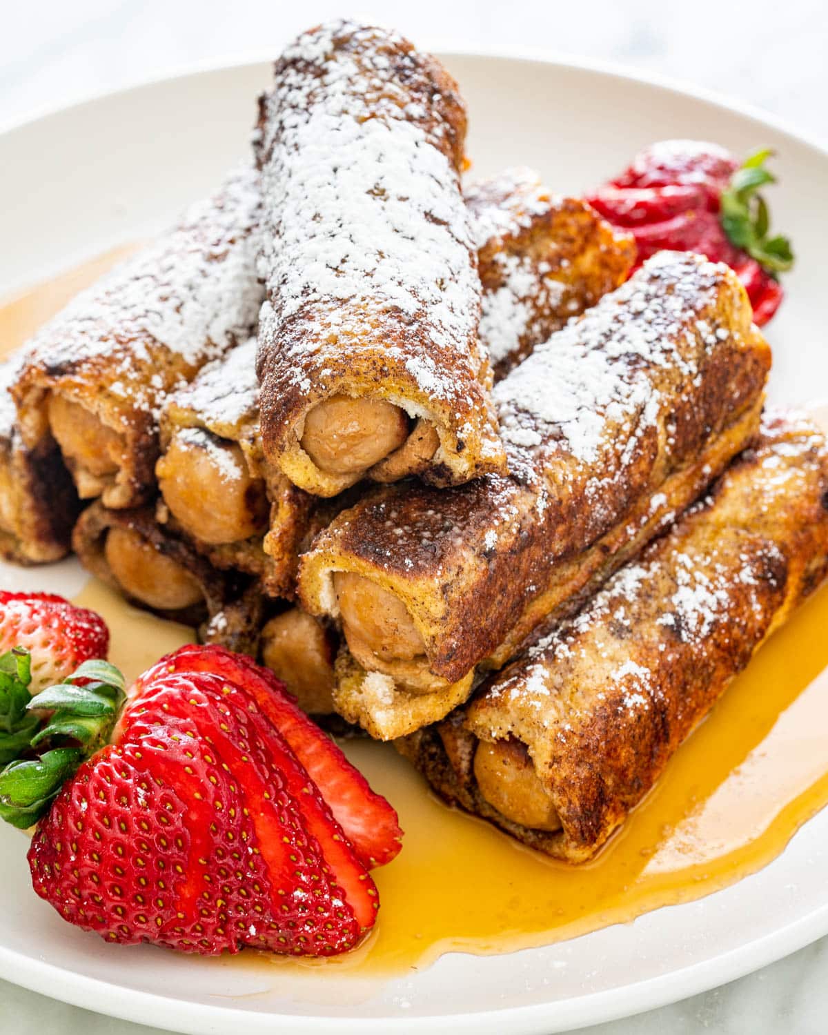 Sausage French Toast Roll Ups on a white plate with strawberries and maple syrup