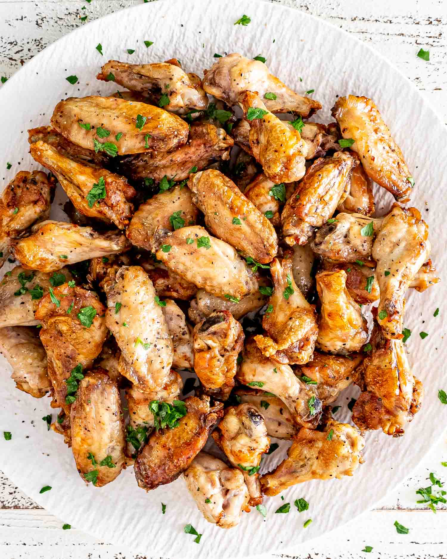 air fryer chicken wings on a round white serving platter garnished with parsley.