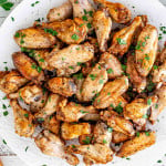 air fryer chicken wings on a round white serving platter garnished with parsley.