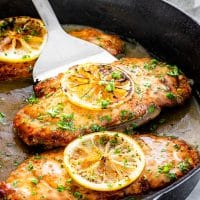 side view shot of chicken francese in a pan, with one being picked up by a spatula