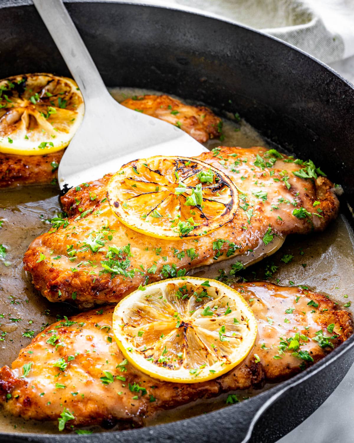 a spatula picking up a piece of chicken francese from a skillet