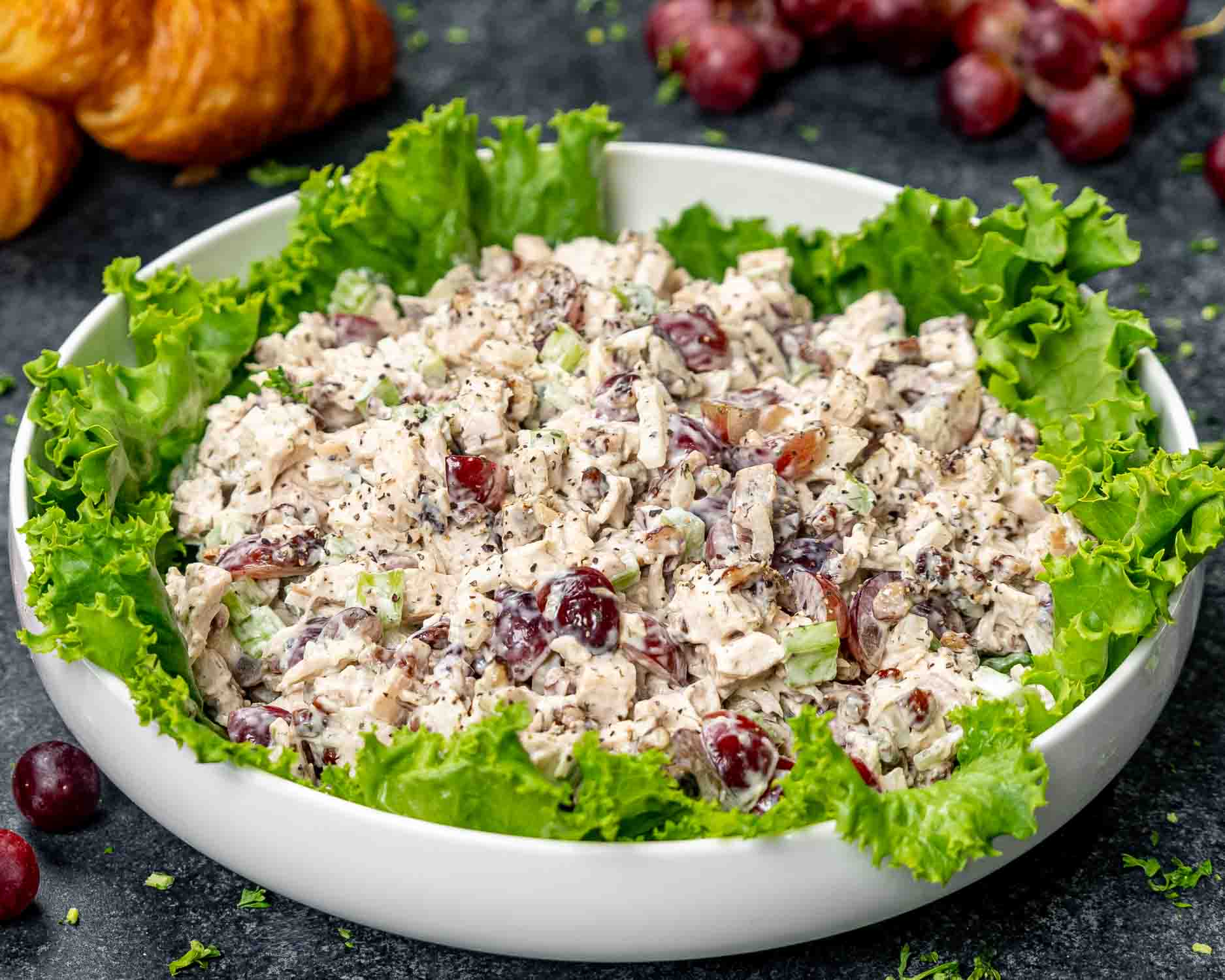 chicken salad in a white bowl lined with lettuce leaves.
