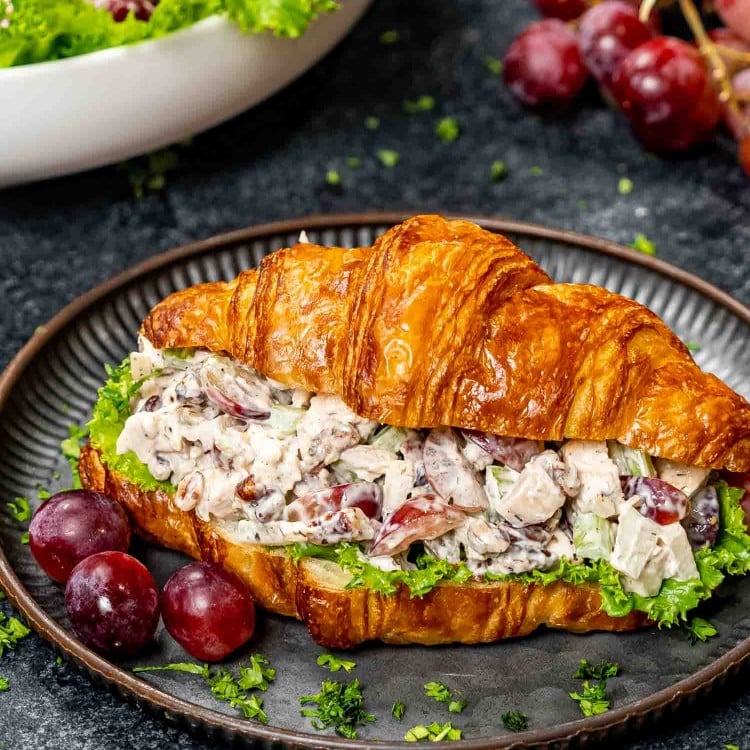 chicken salad on a croissant on a plate with a couple grapes.
