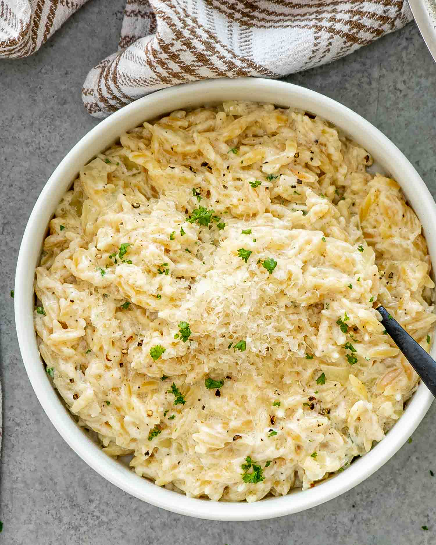 a bowl full of creamy garlic parmesan orzo garnished with a bit of parsley.