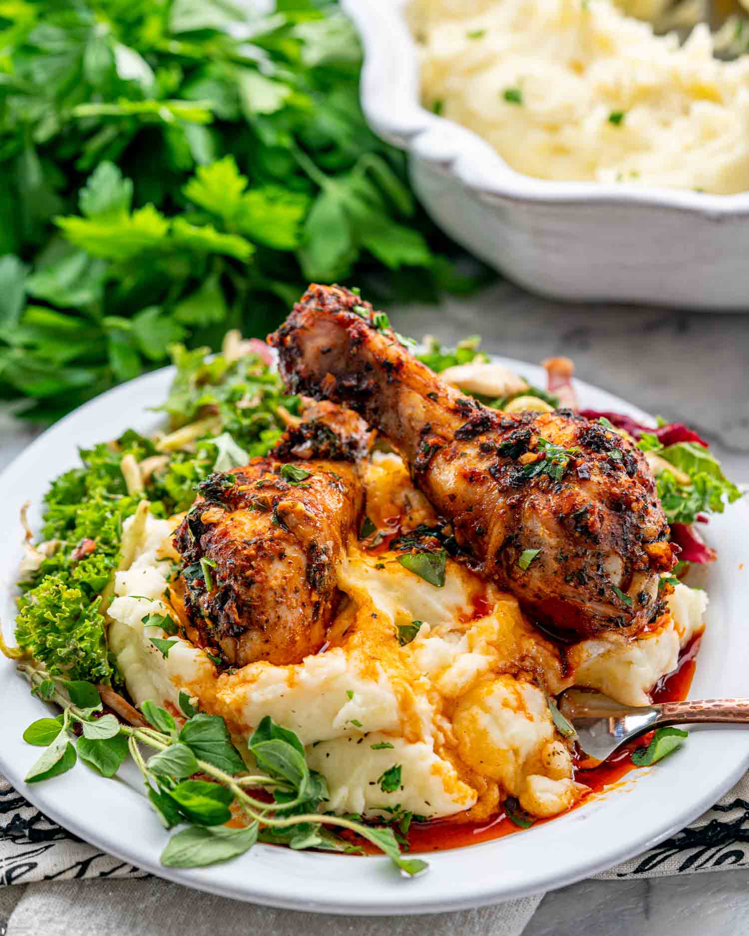 two garlic and paprika chicken drumsticks over a bed of mashed potatoes with a green salad on a white plate.