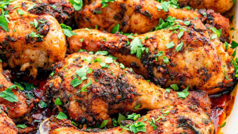 garlic and paprika chicken drumsticks garnished with parsley in a roasting pan.