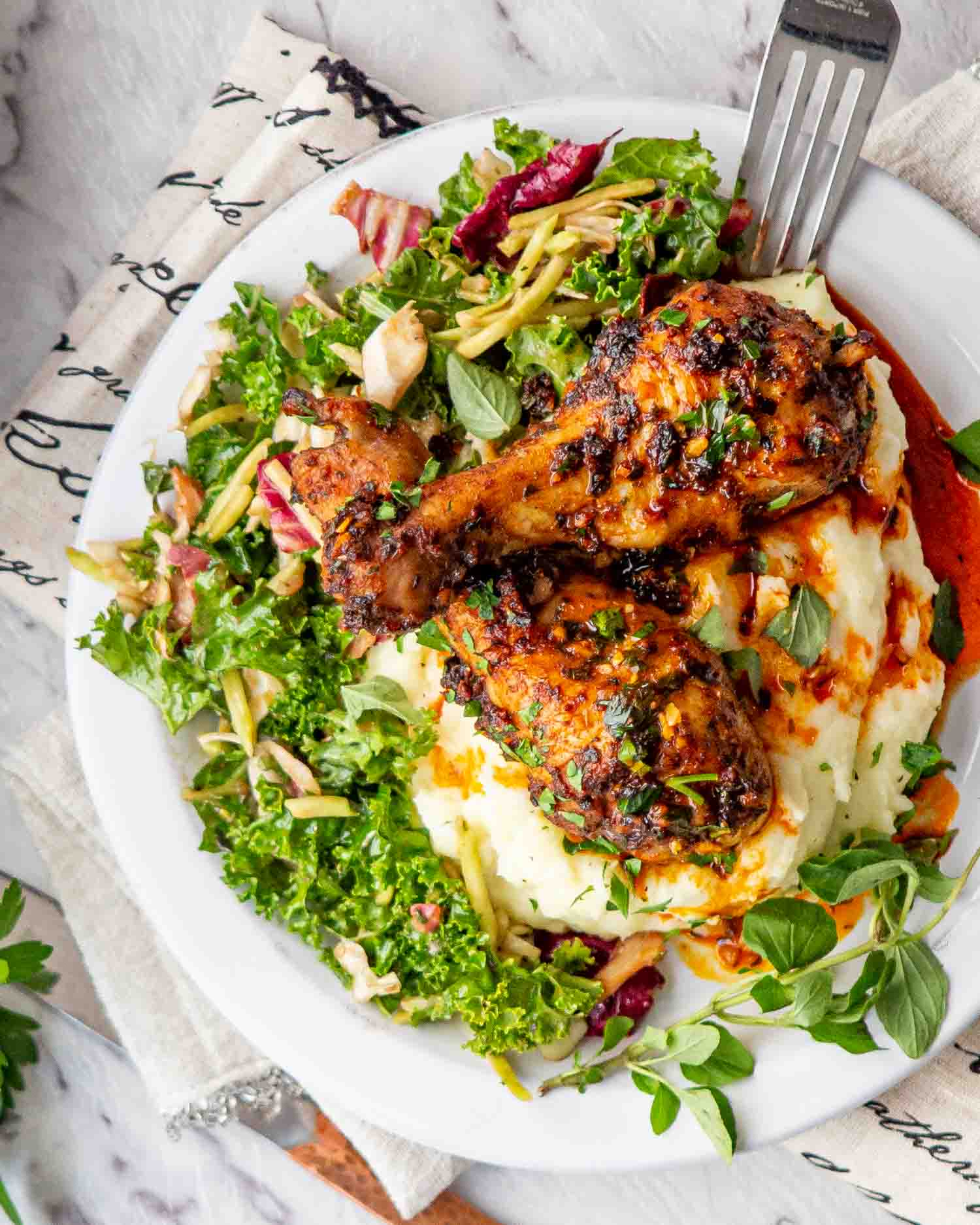 two garlic and paprika chicken drumsticks over a bed of mashed potatoes with a green salad on a white plate.