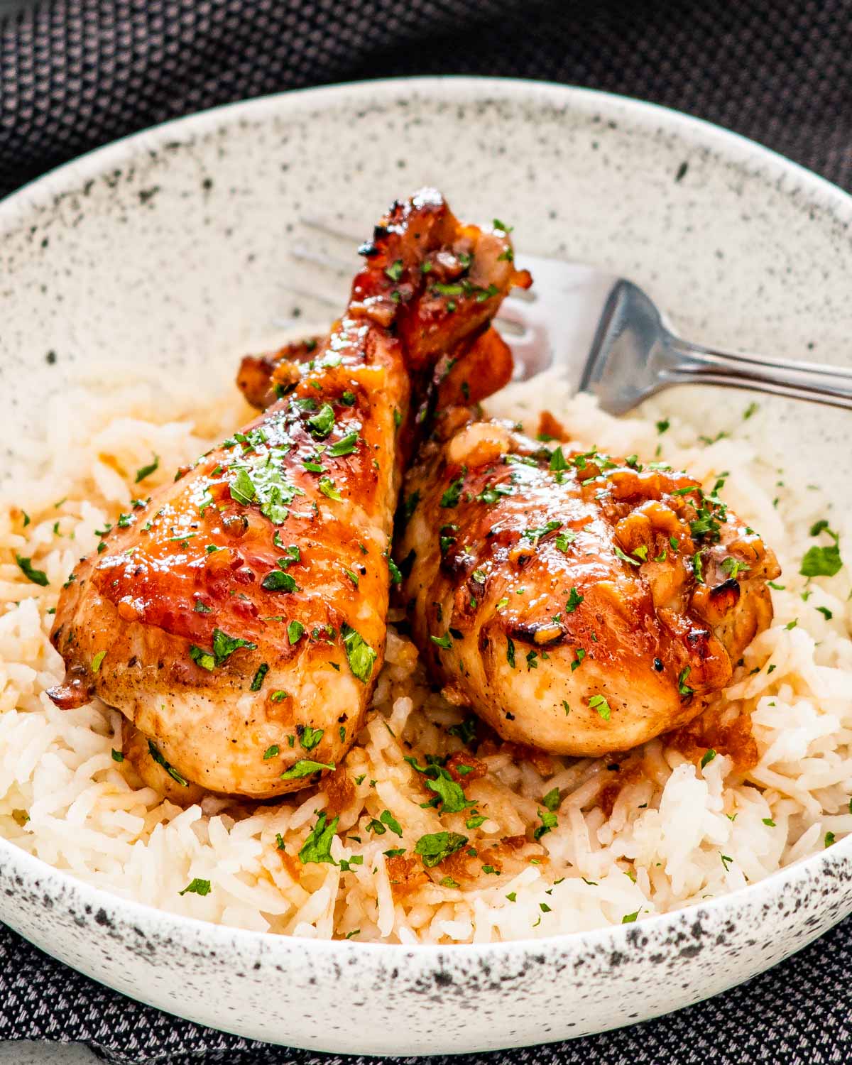 two honey soy chicken drumsticks over a bed of rice garnished with parsley.
