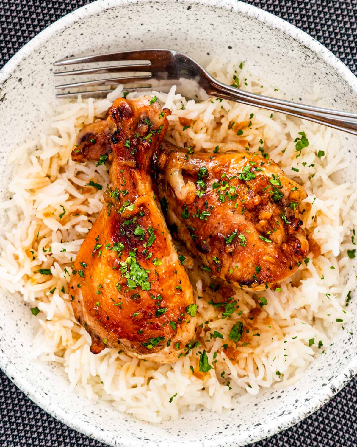 two honey soy chicken drumsticks over a bed of rice garnished with parsley.