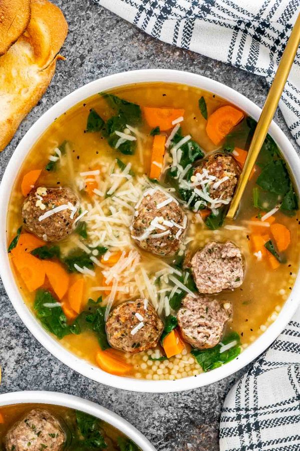 italian wedding soup in a white bowl with a golden spoon.