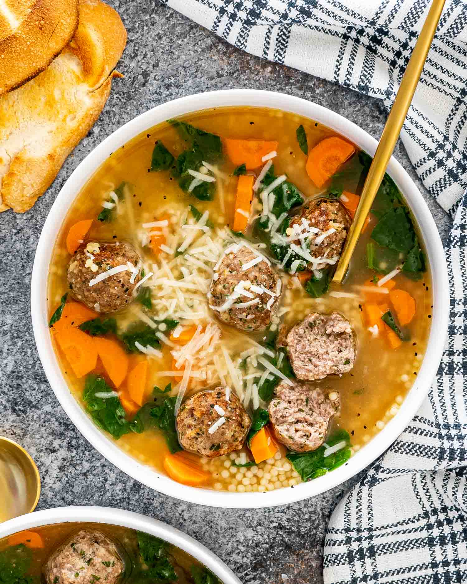 italian wedding soup in a white bowl with a golden spoon.