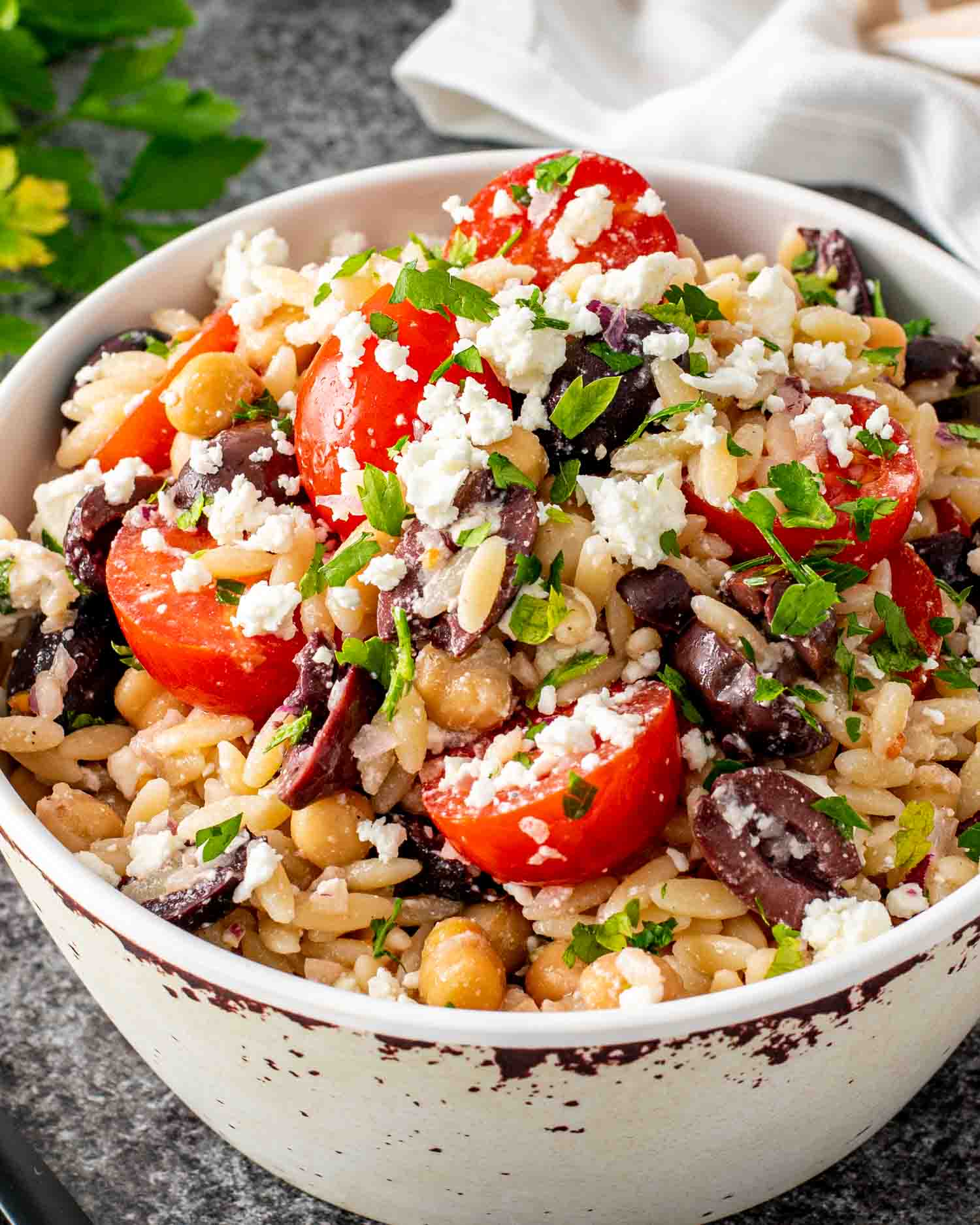 mediterranean orzo salad in a bowl garnished with feta cheese and parsley.
