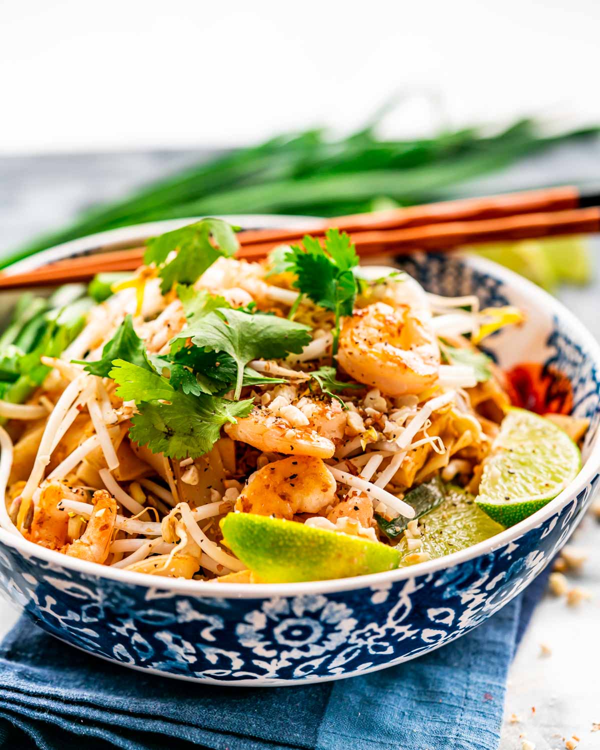 pad thai in a white and blue bowl with chopsticks on the plate.