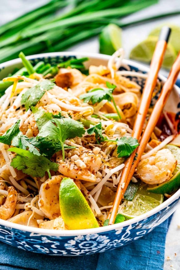 pad thai in a white and blue bowl with chopsticks on the plate.