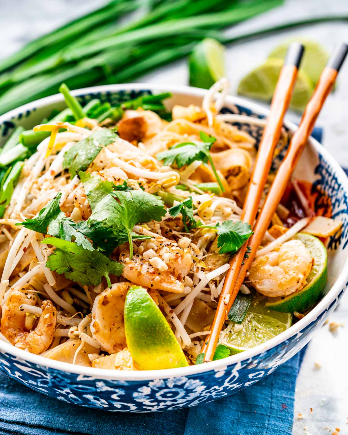 pad thai in a white and blue bowl with chopsticks on the plate.
