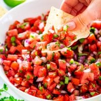 a hand taking a scoop of pico de gallo with a tortilla chip