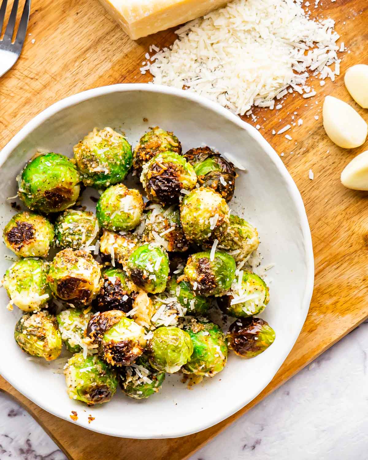 overhead shot of roasted brussels sprouts in a whit bowl next to a block of parmesan cheese.