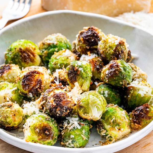 roasted brussels sprouts in a whit bowl next to a block of parmesan cheese.