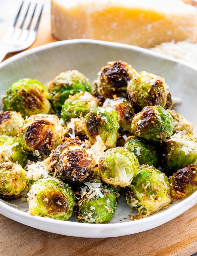 roasted brussels sprouts in a whit bowl next to a block of parmesan cheese.