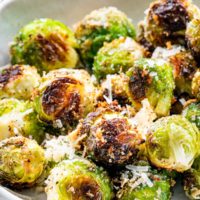 closeup of roasted brussels sprouts in a whit bowl next to a block of parmesan cheese.