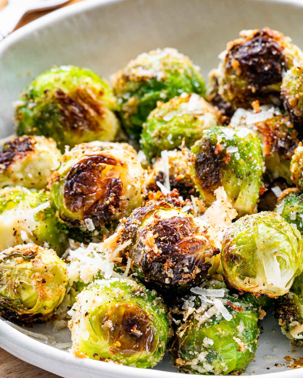 closeup of roasted brussels sprouts in a whit bowl next to a block of parmesan cheese.