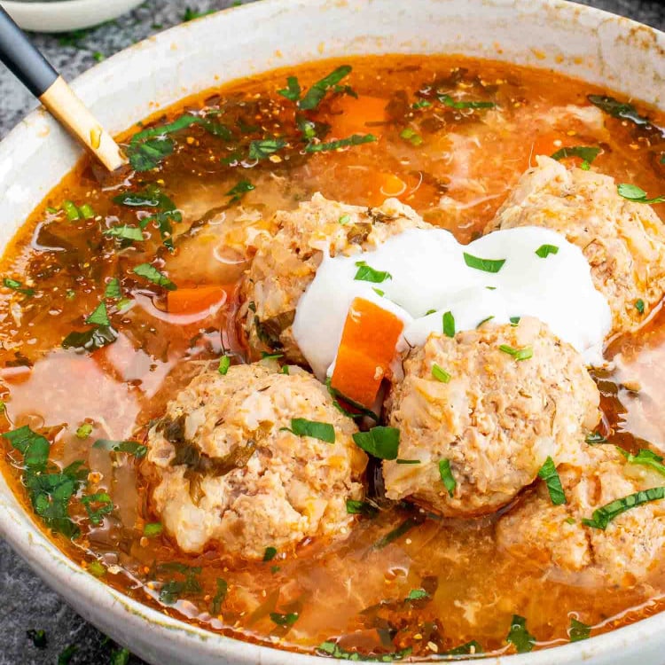 a serving of romanian meatball soup in a bowl with a spoon inside.