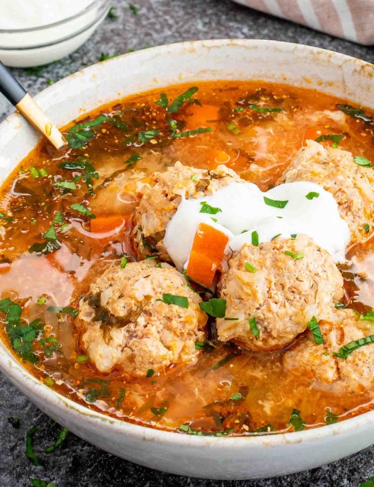 a serving of romanian meatball soup in a bowl with a spoon inside.