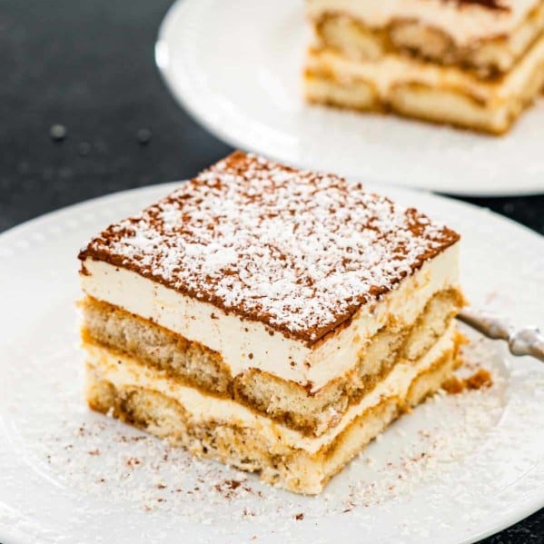 a beautiful slice of tiramisu on a white plate garnished with some shaved chocolate.