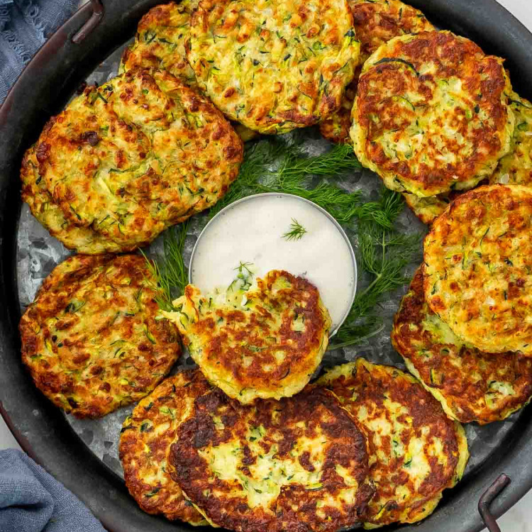 zucchini fritters on a metal plate with a bowl of ranch dressing in the middle.