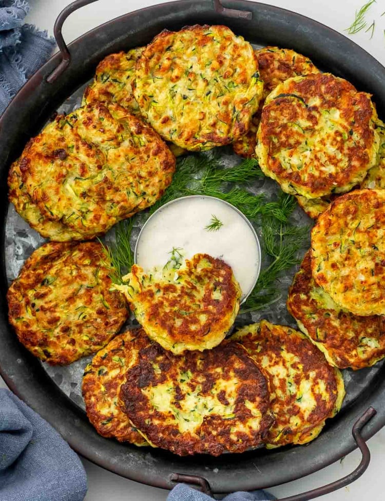 zucchini fritters on a metal plate with a bowl of ranch dressing in the middle.
