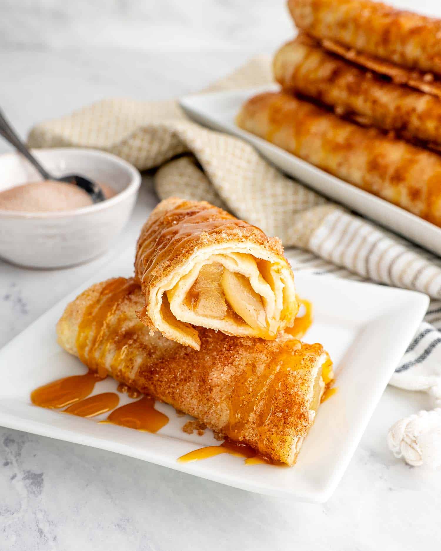 an apple pie taquito drizzled with caramel sauce on a white plate.