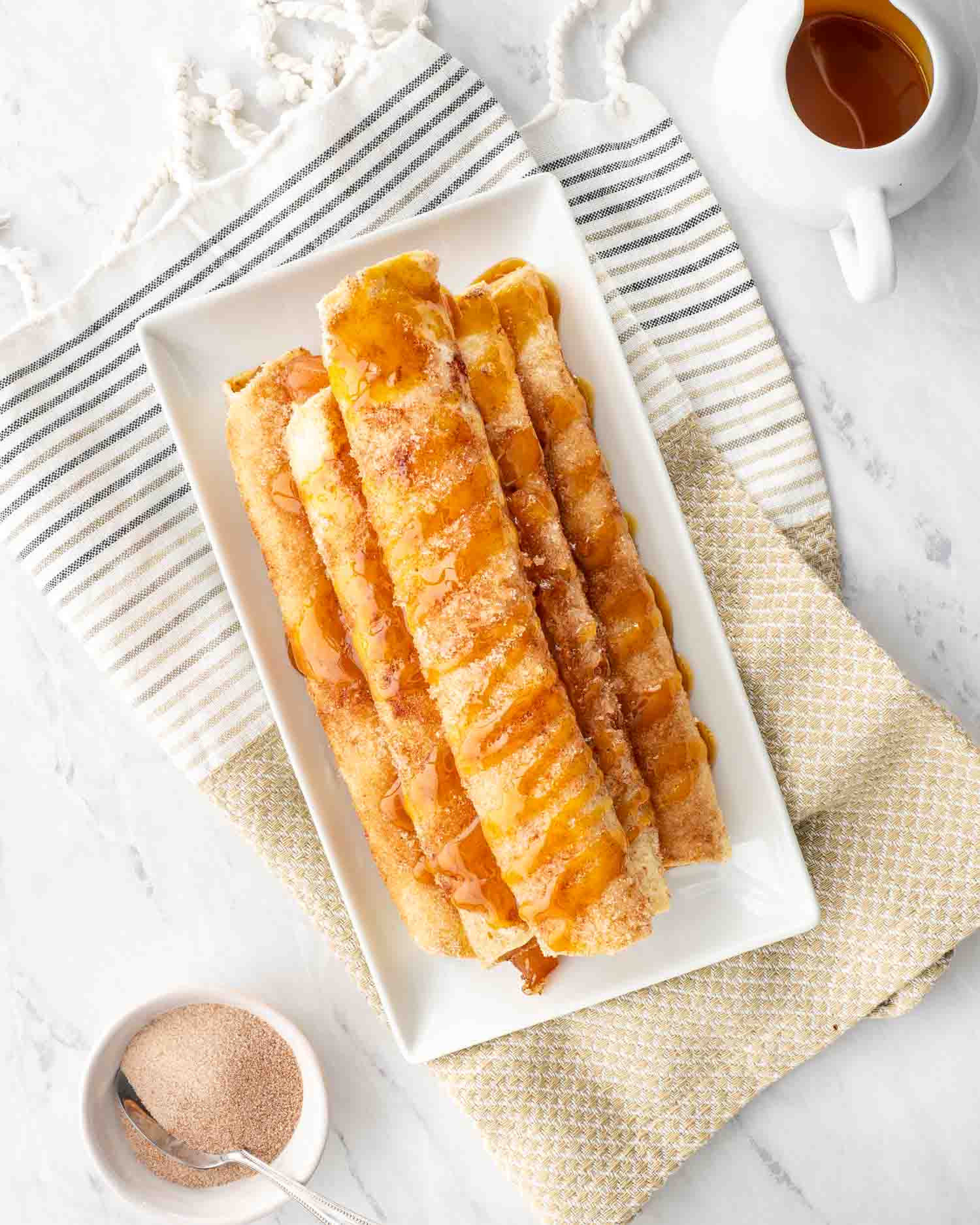 a stack of apple pie taquitos on a white plate drizzled with caramel sauce.