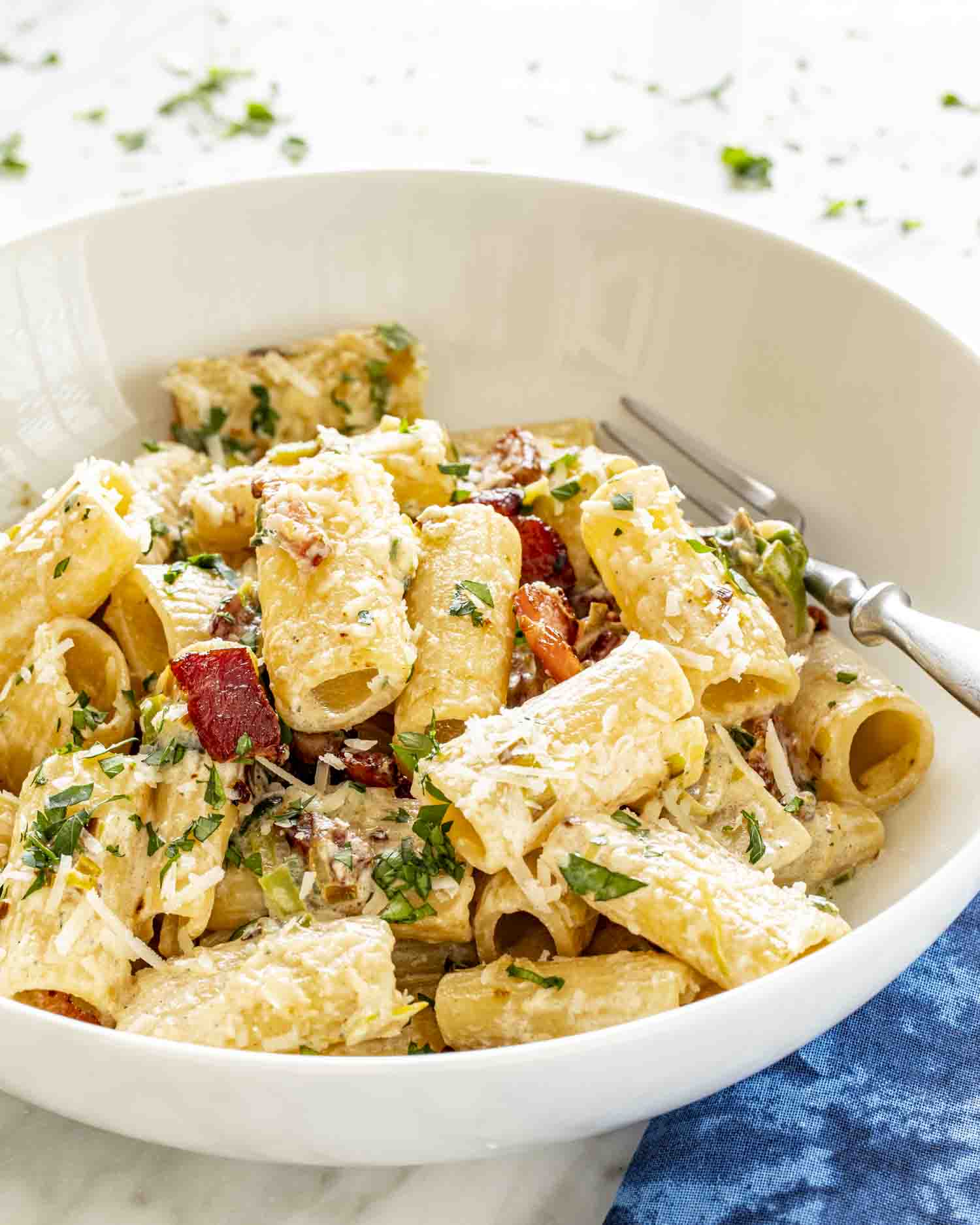a serving of bacon leek pasta in a white bowl.