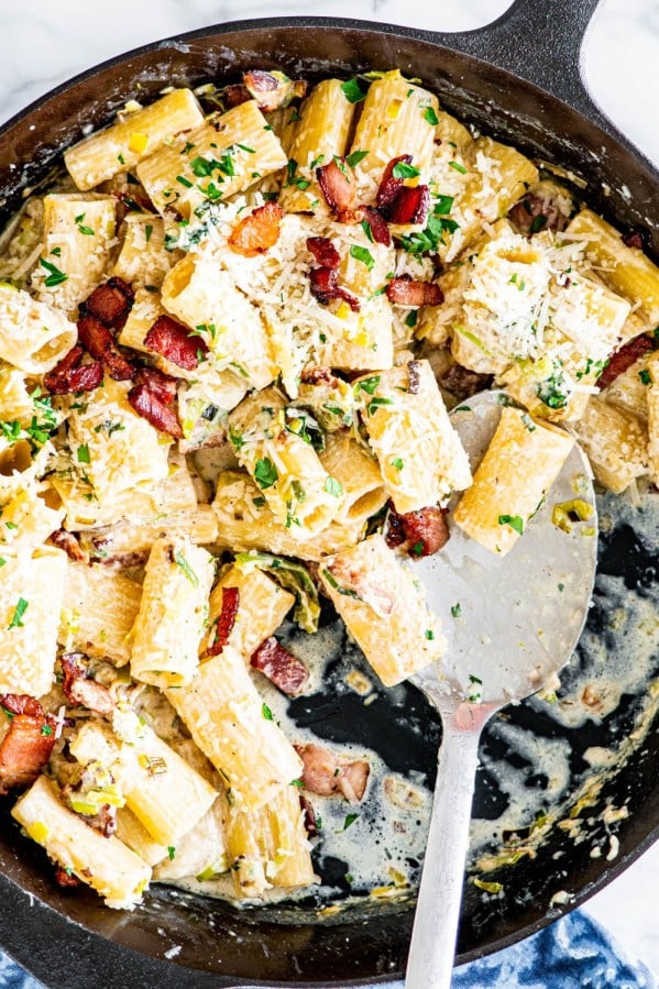 overhead shot of bacon leek pasta in a skillet with a serving spoon in it