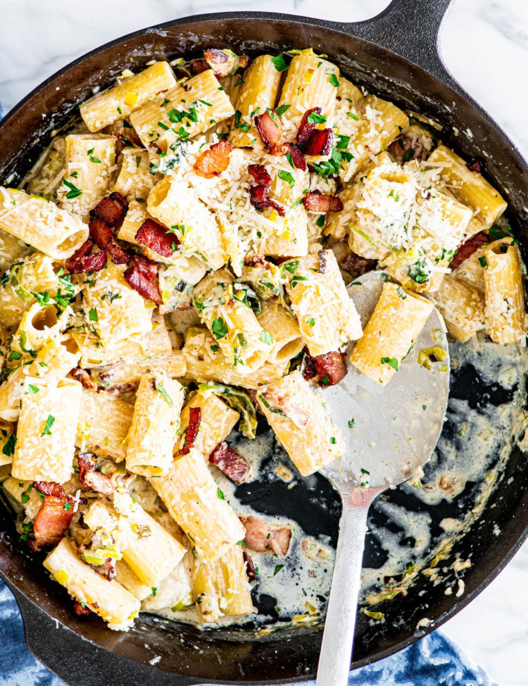 overhead shot of bacon leek pasta in a skillet with a serving spoon in it