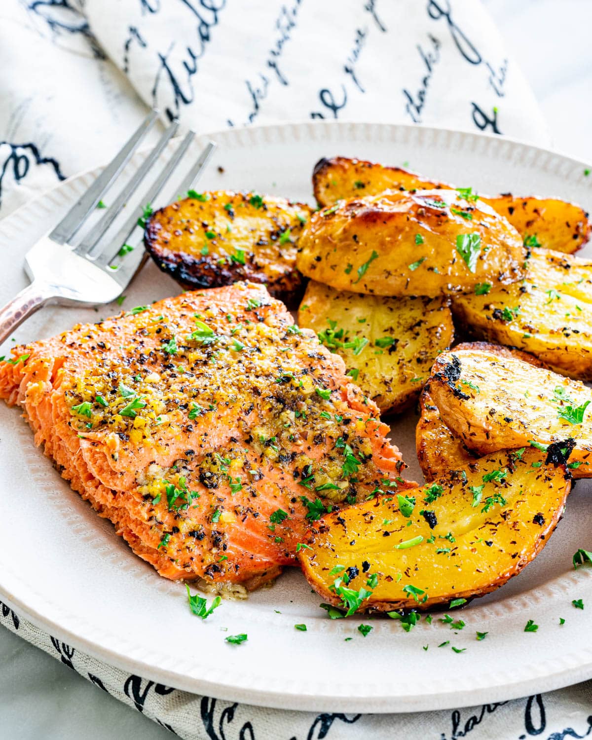 a piece of lemon pepper salmon with roasted potatoes on a white plate