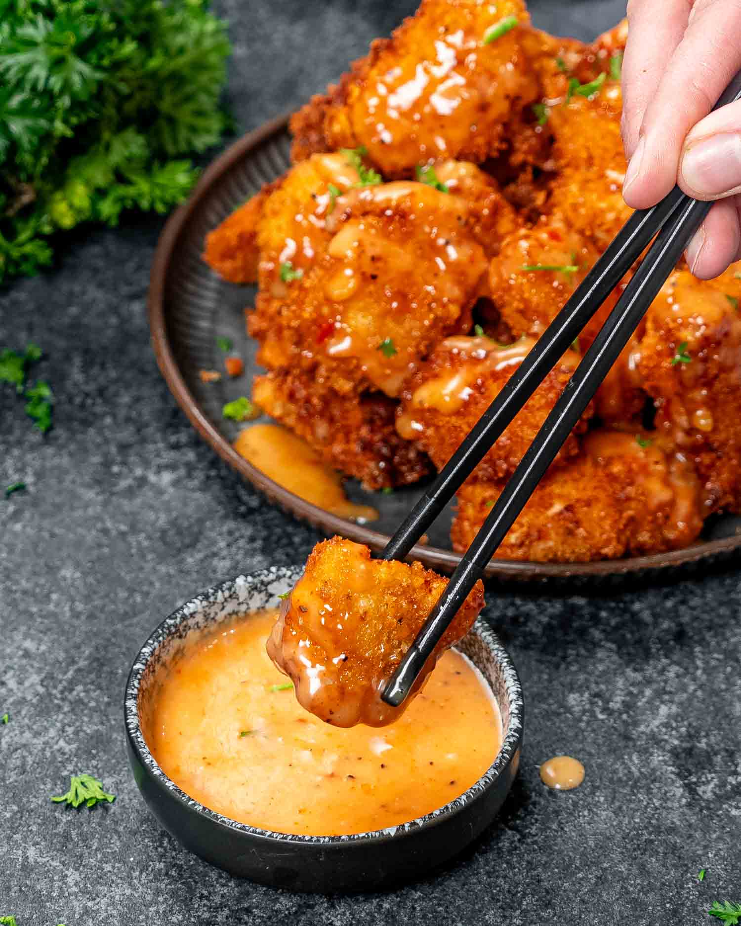 a hand dipping chopsticks holding a bang bang chicken piece in a bowl with bang bang sauce.