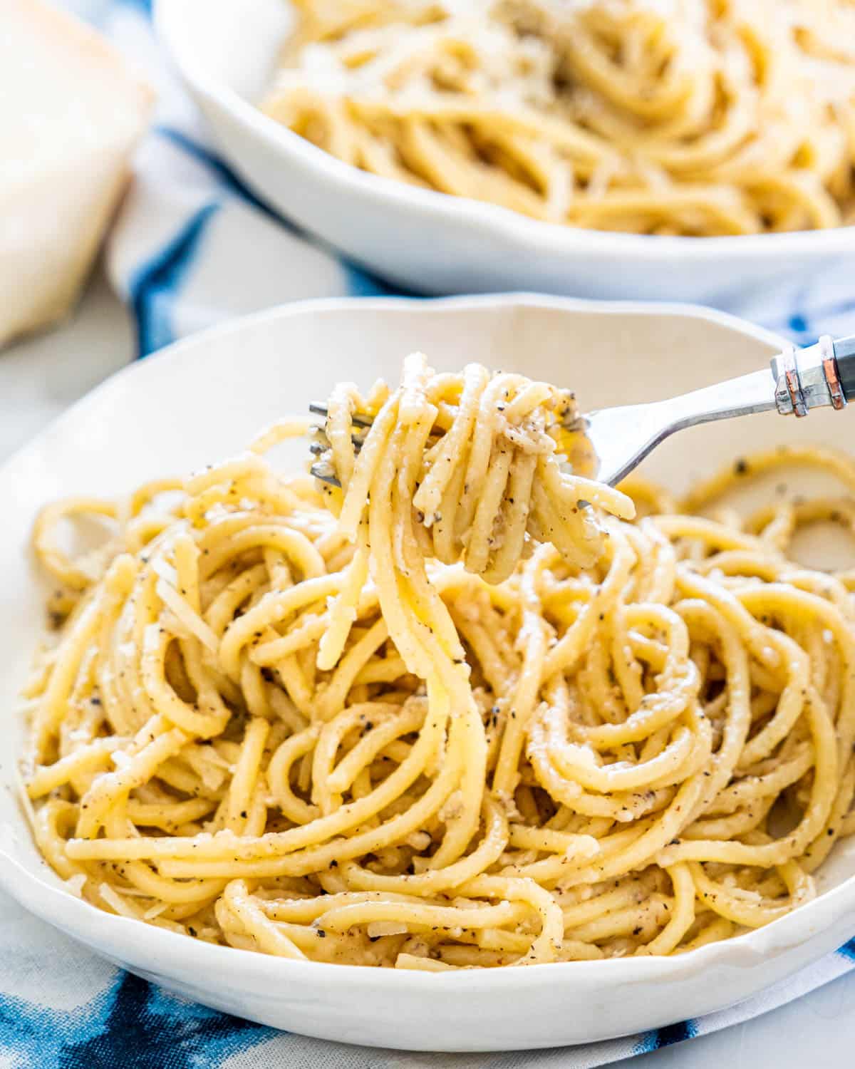 Cacio e Pepe in 2 white plates with a fork twirling pasta