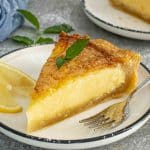 Close view of lemon chess pie slice with creamy custard center and crisp crust served with lemon slices and mint.