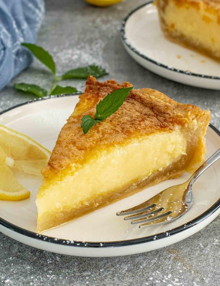 Close view of lemon chess pie slice with creamy custard center and crisp crust served with lemon slices and mint.