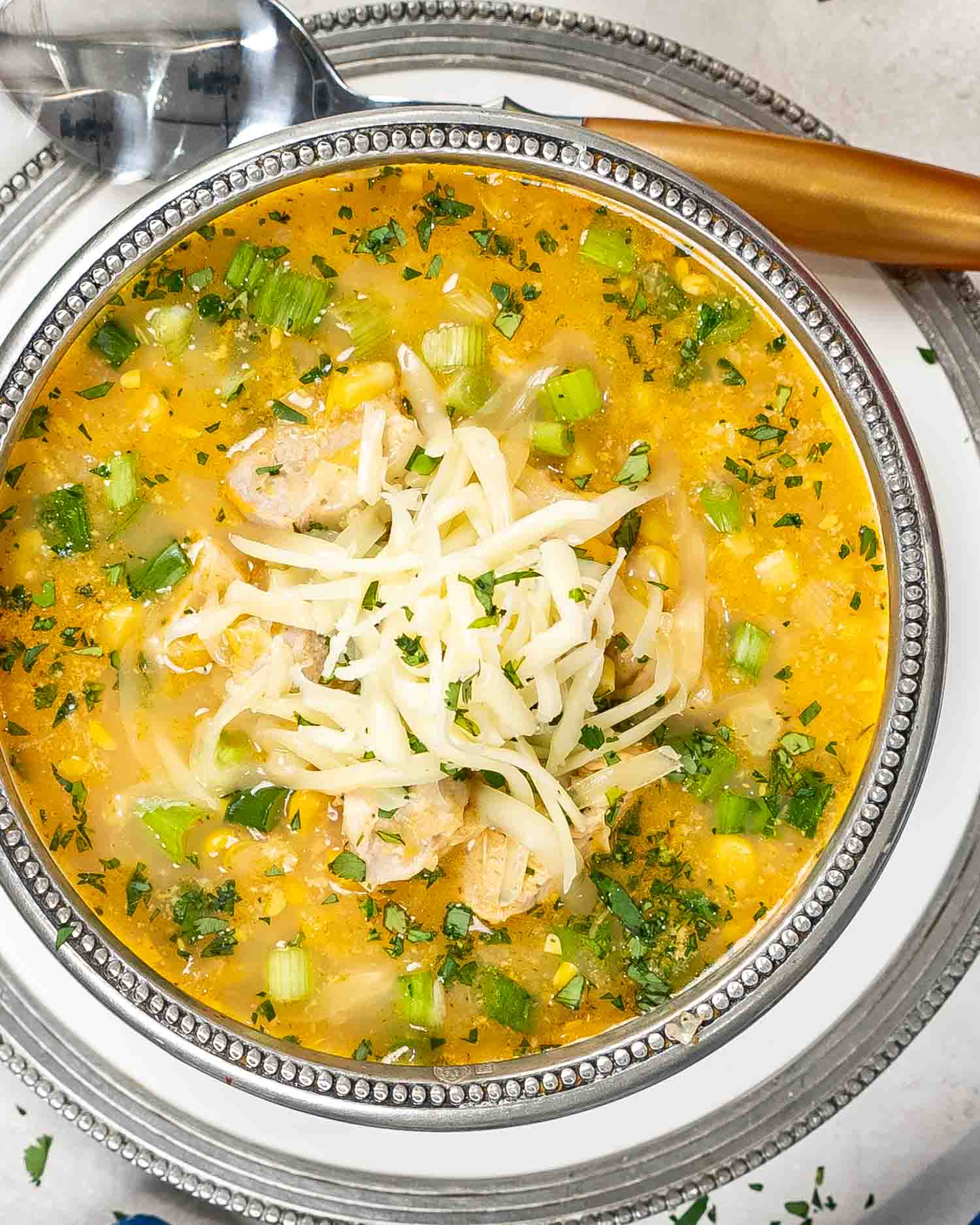 a bowl of chicken and corn chowder with monterey jack cheese and garnished with cilantro and green onions.