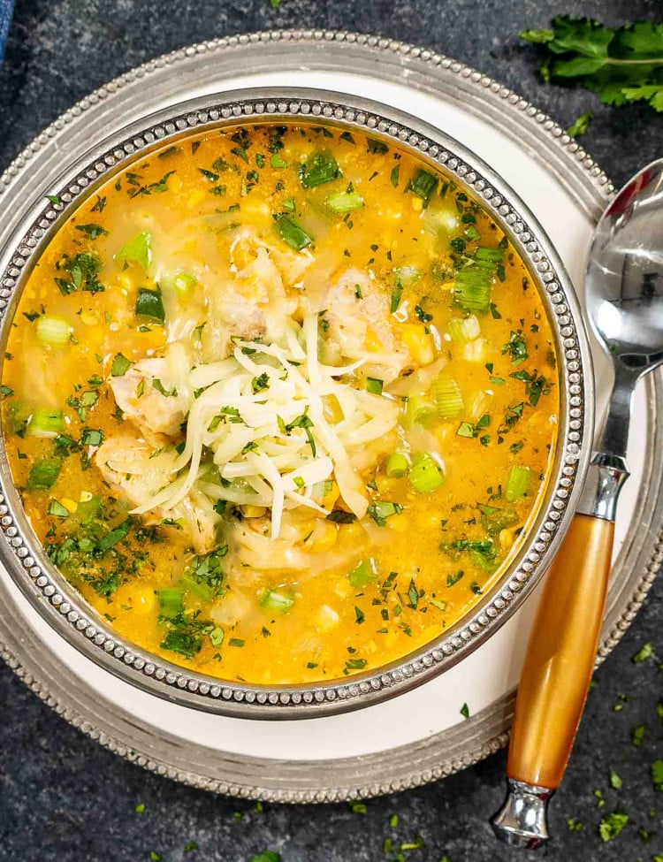 a bowl of chicken and corn chowder with monterey jack cheese and garnished with cilantro and green onions.