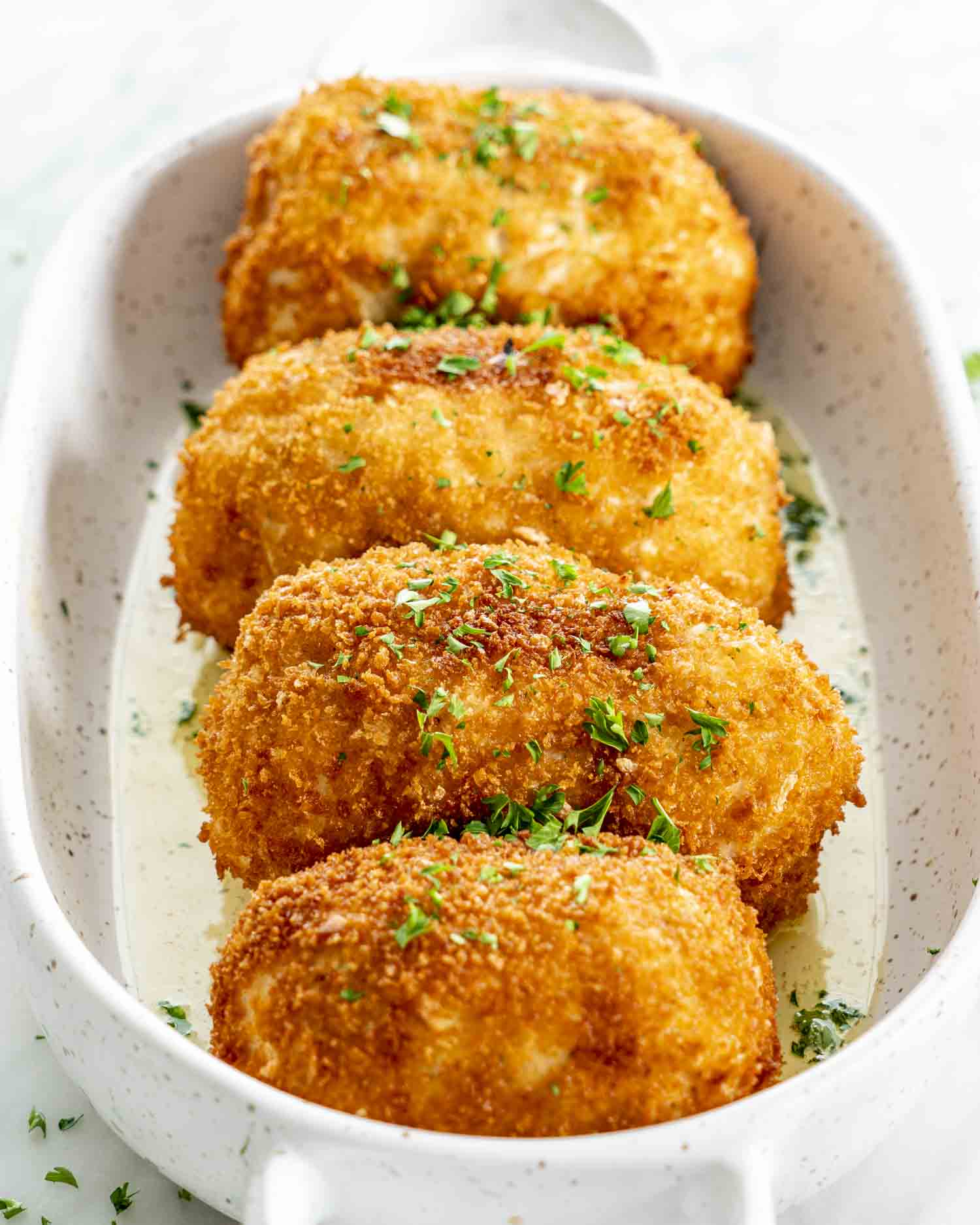 Chicken Kiev Four golden, crispy Chicken Kievs garnished with parsley, arranged neatly in a glass baking dish.